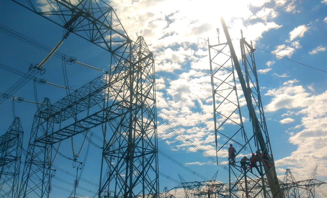 Steel structures under the blue sky and clouds, with men working at heights wearing their personal protection equipment.