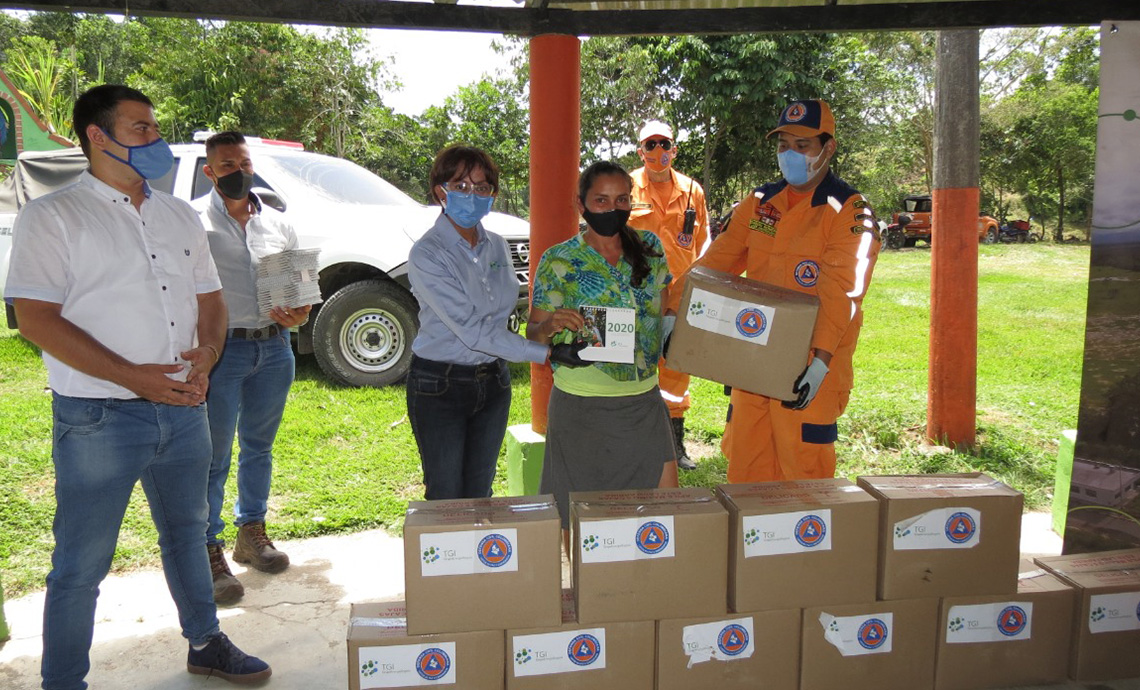 una mujer posa con la caja con ayudas humanitarias al lado de una mujer del personal de TGI y un hombre de la Defensa Civil.
