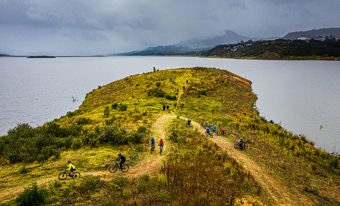 lago rodeado de montañas, ciclistas andan por la orilla.