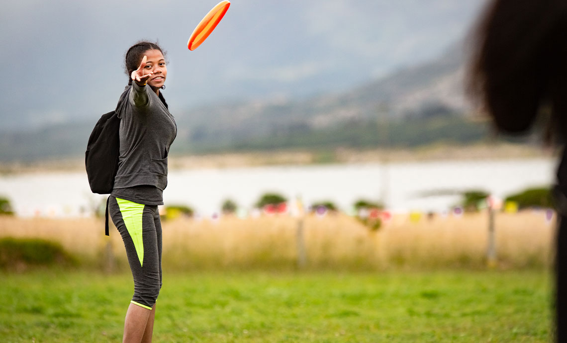 una joven con ropa deportiva lanzando un frisbee al lado de un lago.